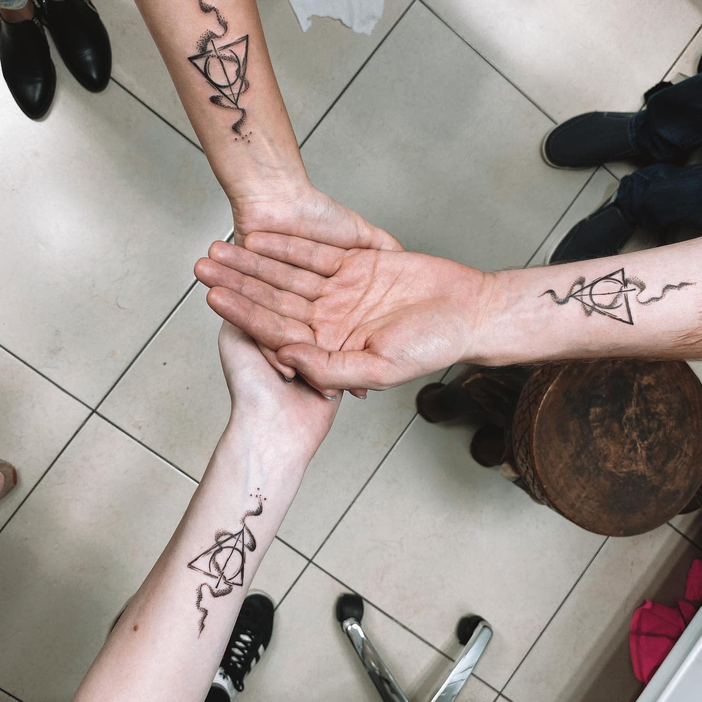 Three forearms with matching geometric tattoos forming a triangle